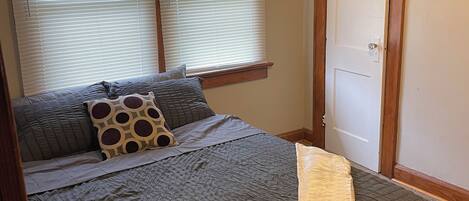 A bedroom with a bed, two windows with blinds, a door, and a ceiling fan.