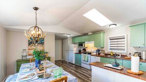 A modern kitchen with green cabinets, a dining table set with plates and glasses, and a chandelier. - Beaver Lodge - 33 Acres of Secret Getaway, House with AC, RV Parking (Wetaskiwin)