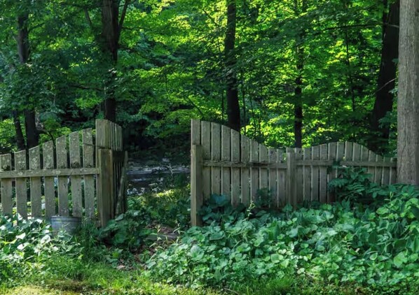 A wooden gate in a forested area with dense greenery and trees. - Historic, beautifully renovated riverside apartment in North Ferrisburgh (Ferrisburgh)