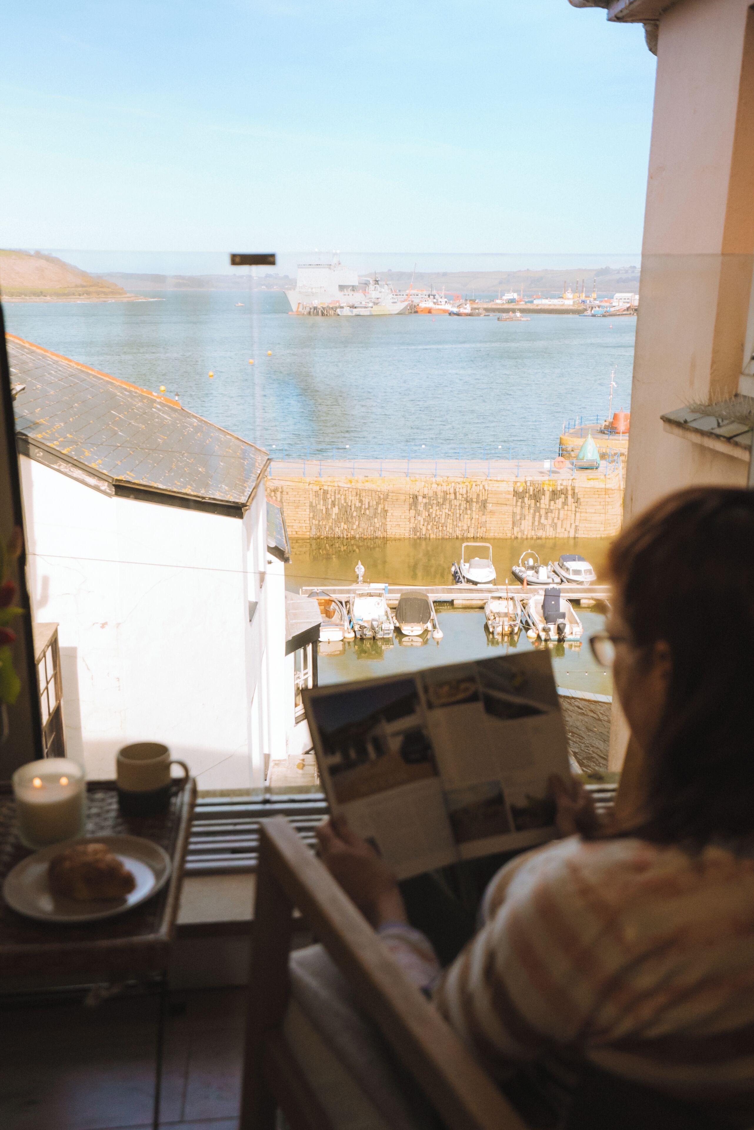 Eine Person liest eine Zeitschrift an einem Tisch mit Blick auf einen Hafen und Boote.