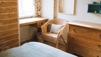A bedroom with a wooden desk, a wicker chair, a bed, and a dresser.