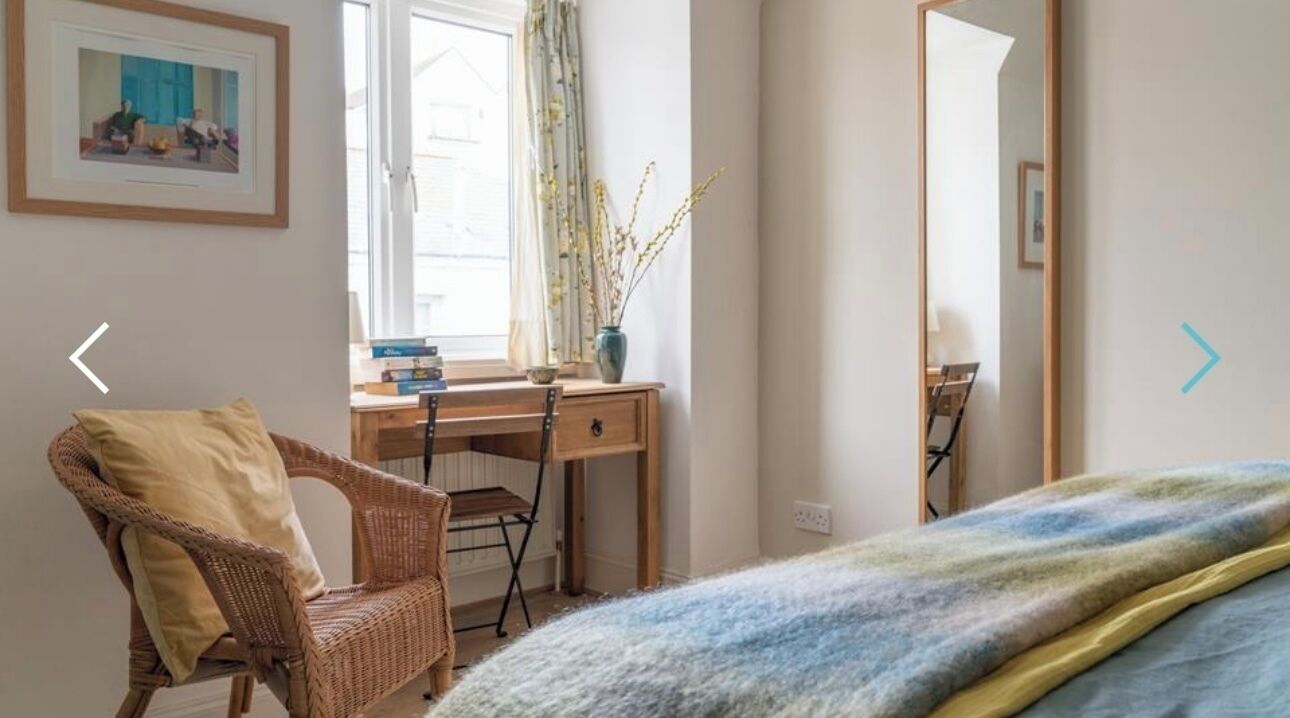 Un dormitorio con cama, escritorio, silla y ventana con cortinas.