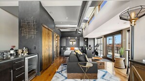 A modern hotel room with a kitchenette, a large bed, a sofa, and a view of the outdoors. - Penthouse With Mountain Views in Heart of Old Town (Fort Collins)