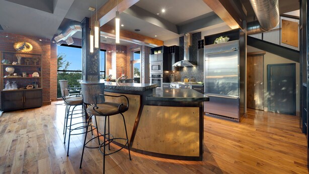 A modern kitchen with a central island, bar stools, stainless steel appliances, and a brick accent wall. - Penthouse With Mountain Views in Heart of Old Town (Fort Collins)