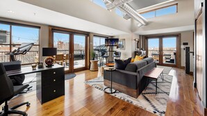 A spacious living area with a large window, a modern desk, a sofa, and a dining table. - Penthouse With Mountain Views in Heart of Old Town (Fort Collins)