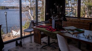 Une pièce chaleureuse avec une grande fenêtre donnant sur un lac, une table en bois sur laquelle est disposé un jeu d’échecs, et un banc.
