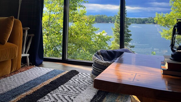 Une pièce dotée de grandes fenêtres donnant sur un lac, avec une table en bois, une lampe et un canapé.