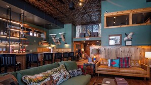 Un intérieur chaleureux avec un canapé vert, des éléments décoratifs en bois, un coin bar et un plafond rustique.