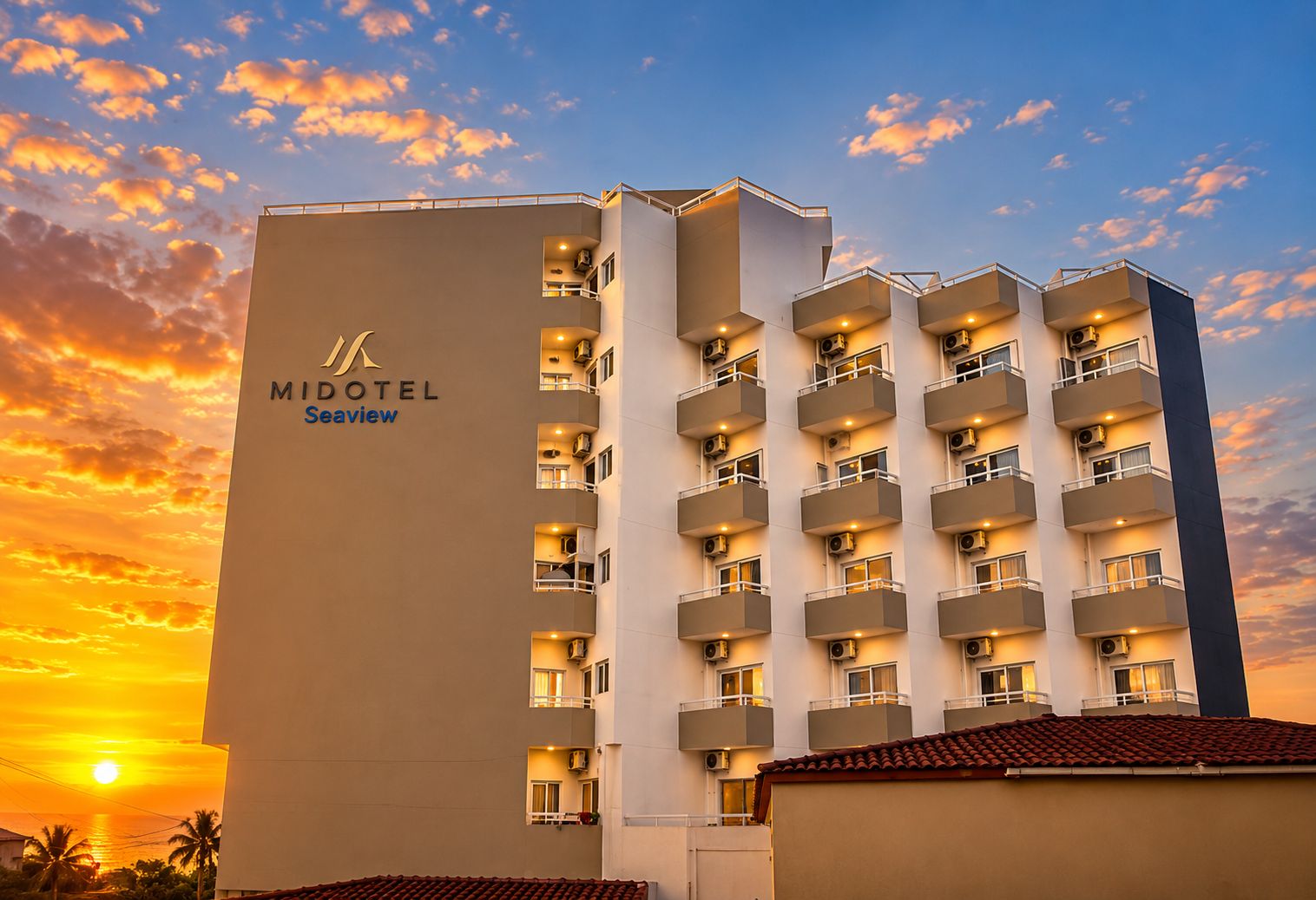 Un hotel a più piani con balconi, un logo ben visibile e un cielo al tramonto.