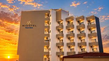 Un hotel a più piani con balconi, un logo ben visibile e un cielo al tramonto.