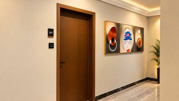 Un pasillo de hotel con una puerta de madera, un cartel con el número de habitación y arte abstracto en la pared.