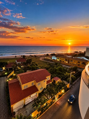 A coastal residential area with houses, a road, and a sunset over the ocean. - Hotel Midotel Seaview (Pointe-Noire)