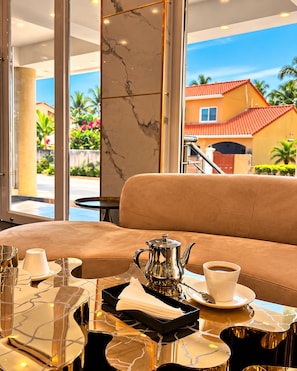 A modern interior with a sofa, a table with a coffee setup, and a view of a residential area. - Hotel Midotel Seaview (Pointe-Noire)