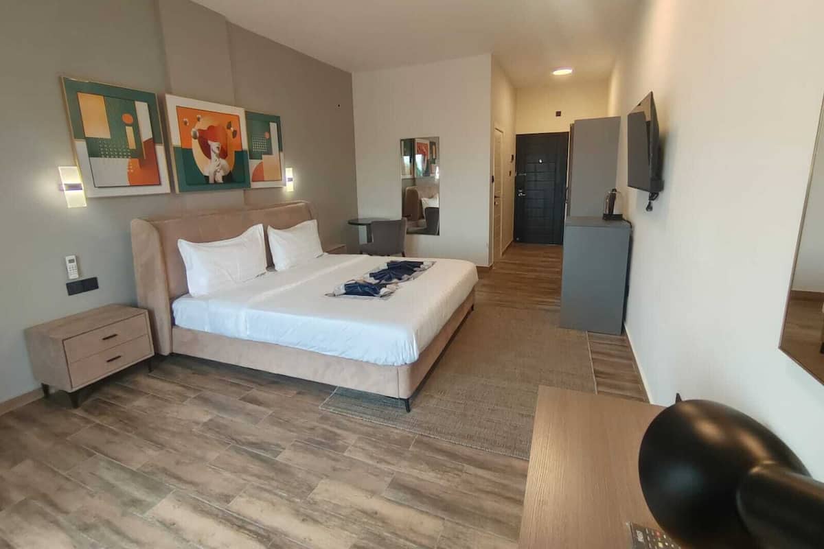 A modern hotel room with a large bed, a desk, a chair, and a TV.