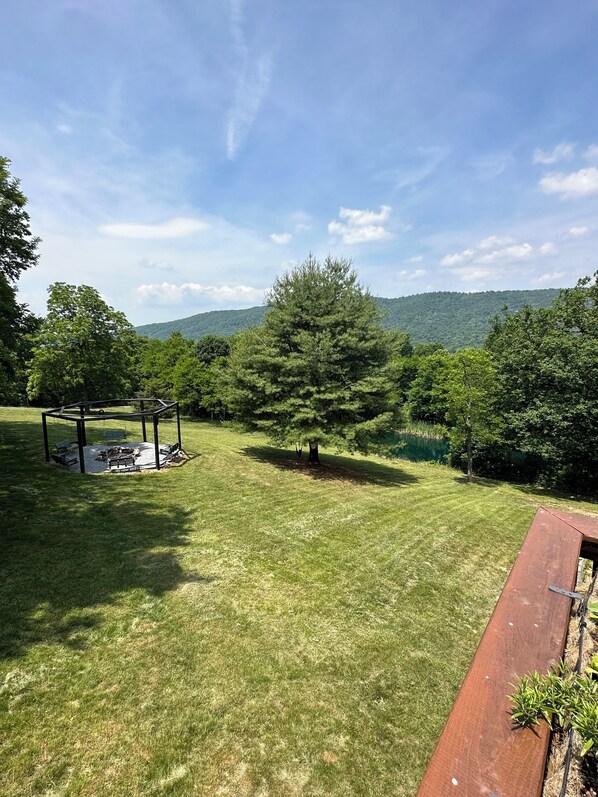 A grassy outdoor area with a wooden structure, trees, and a hilly landscape in the background.