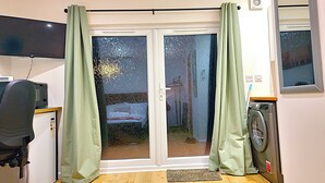 Een kamer met een schuifglazen deur naar een balkon, een wasmachine, een magnetron en een klein bureau met stoel.