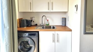 Een kleine keuken met een wasmachine, een koffiezetapparaat en een spoelbak.