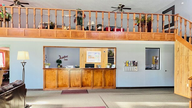 A reception area with a wooden desk, a sign reading "The Ashley Inn," and a staircase leading to an upper level. - The ashley inn (Crossett)