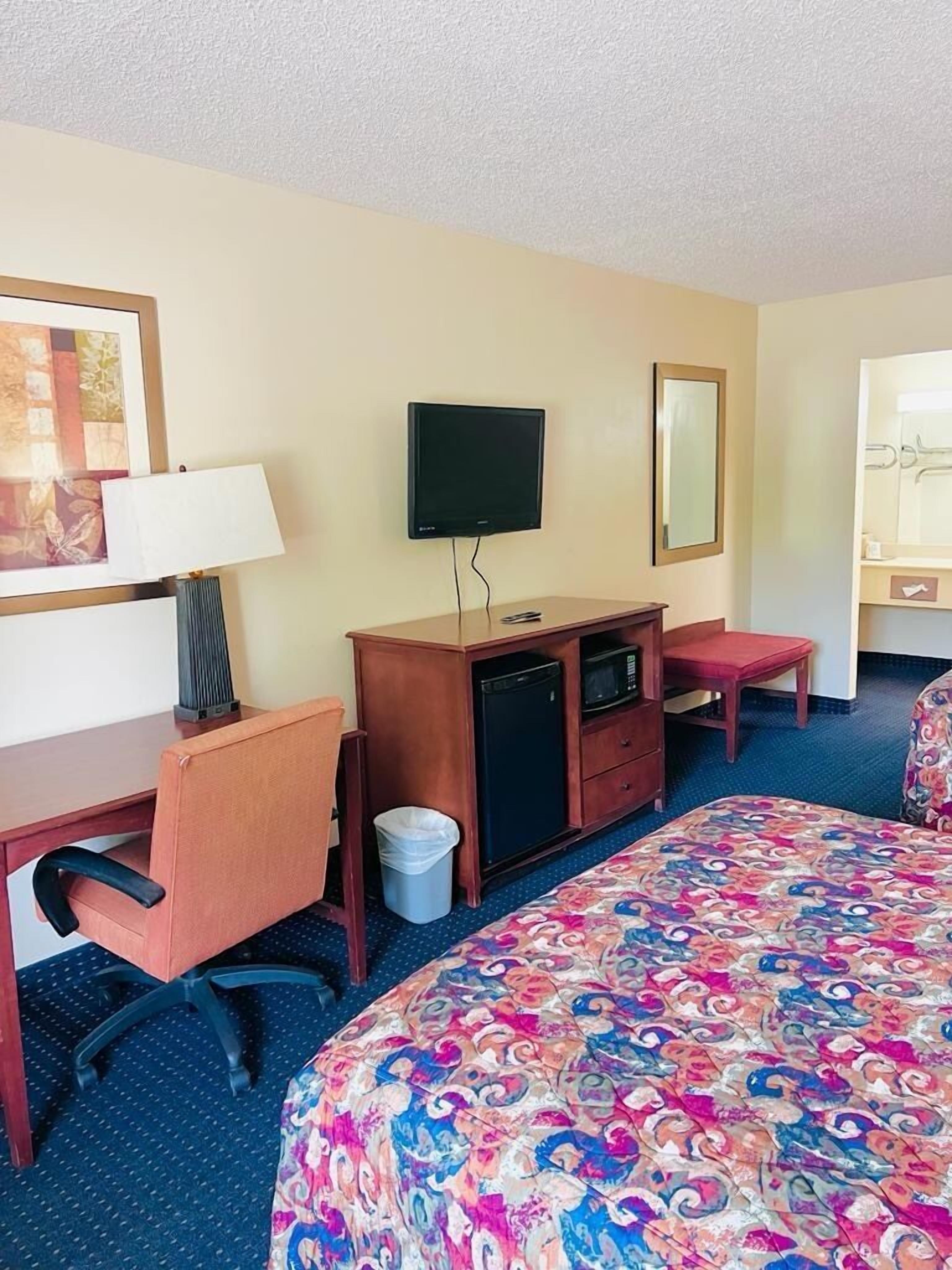 Una habitación de hotel con cama, escritorio, silla, televisor y un refrigerador pequeño.