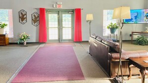 A lobby with a red carpet, a clock, a sofa, a TV, and an exit sign. - The ashley inn (Crossett)