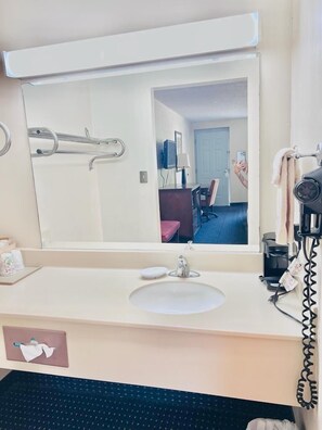 A hotel bathroom with a large mirror, a sink, a towel rack, and a hairdryer. - The ashley inn (Crossett)