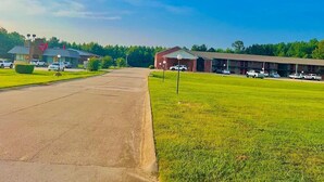 A parking lot with a building on the left and a grassy area with another building on the right. - The ashley inn (Crossett)