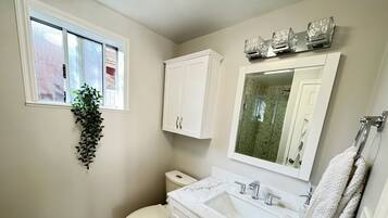 A bathroom with a toilet, sink, and cabinets. There is a window with a plant hanging from it.