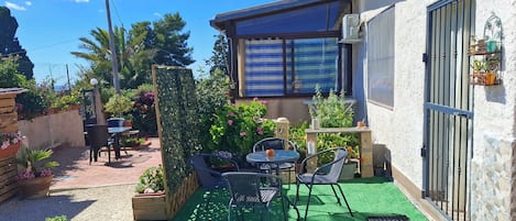 A patio with a table and chairs, surrounded by potted plants and a green artificial turf.