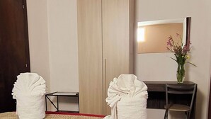 A hotel room with a bed, two towels, a desk, a chair, a mirror, and a vase with flowers.