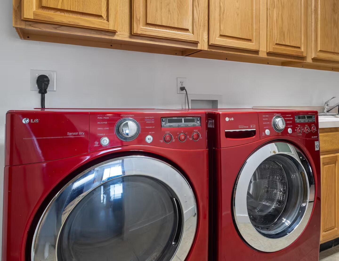 Two red LG Sensor Dry front-loading washing machines in a kitchen with wooden cabinets and a white countertop.