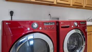 Two red LG Sensor Dry front-loading washing machines in a kitchen with wooden cabinets and a white countertop.