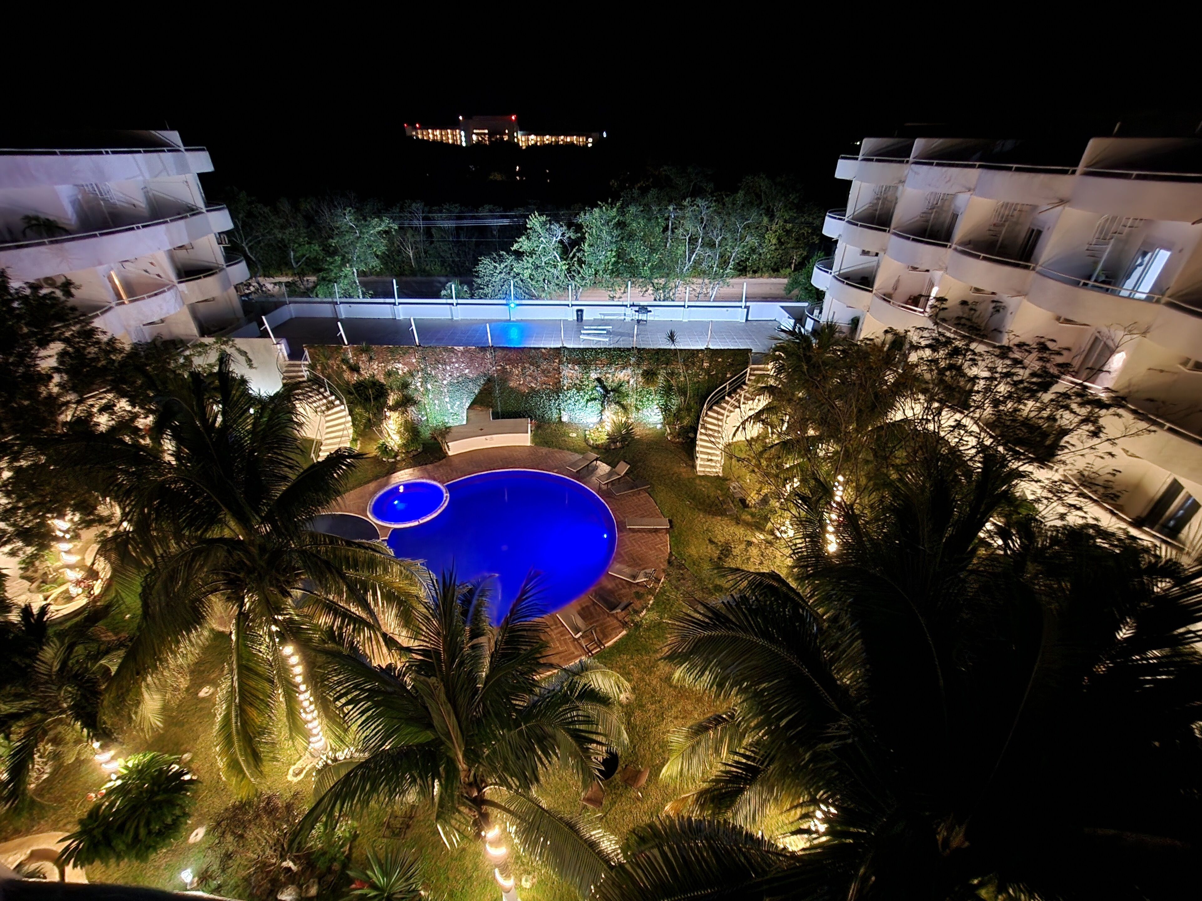 Natten over et hotel med swimmingpool, omgivet af palmer og et velbelyst udendørsområde.