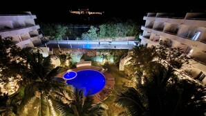 Ein Hotel bei Nacht mit Schwimmbecken, umgeben von Palmen und einem gut beleuchteten Außenbereich.
