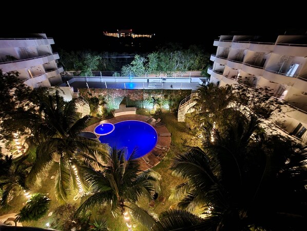 A nighttime view of a hotel with a swimming pool surrounded by palm trees and a well-lit outdoor area.