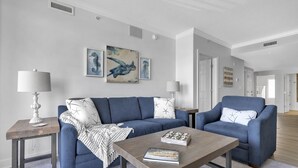 A living room with a blue sofa, a coffee table, and a lamp on a side table. - Boardwalk to Beach ready! Boat Slip & Parking. (Ocean City)