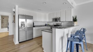 A modern kitchen with white cabinets, stainless steel appliances, a granite countertop, and blue bar stools. - Boardwalk to Beach ready! Boat Slip & Parking. (Ocean City)