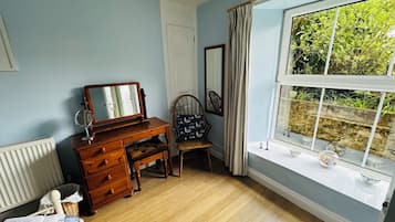 Een kamer met een houten dressoir, een stoel, een raam met uitzicht op groen en een radiator.