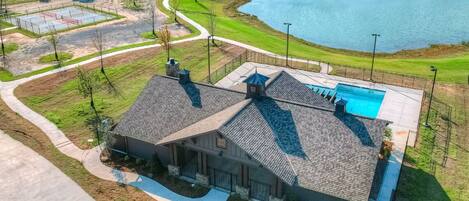 A large house with a swimming pool, a tennis court, and a pond.