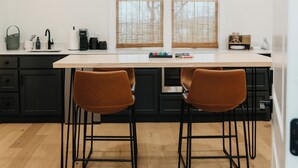 Una cocina moderna con dos taburetes de bar, encimera blanca y suelo de madera.