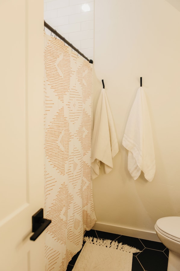 A bathroom with a shower curtain, two towels hanging on hooks, a toilet, and a hexagonal tile floor.