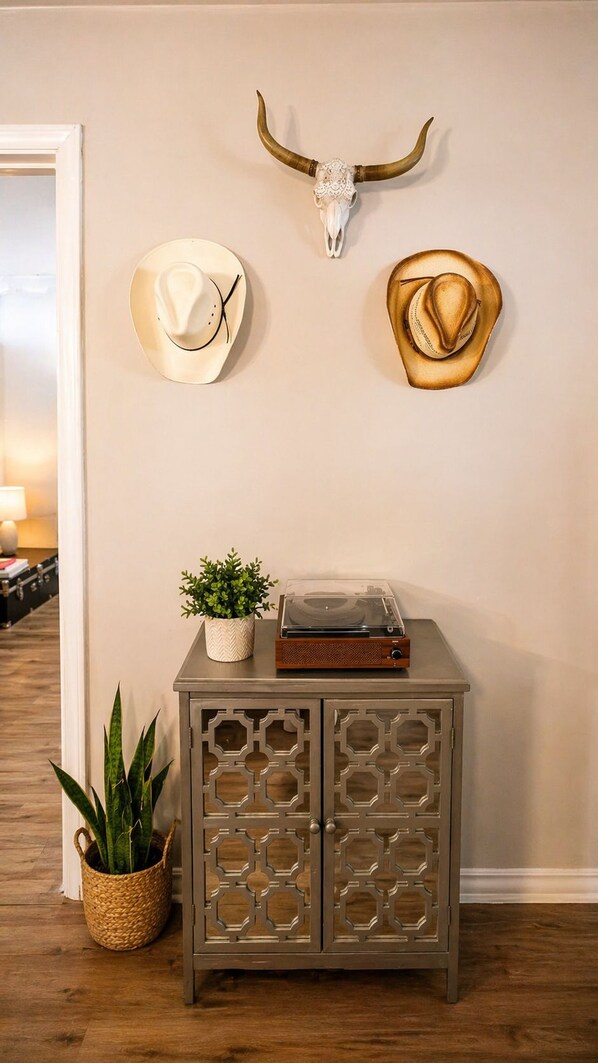 Una pared con un cráneo colgado, dos sombreros de vaquero, un tocadiscos y un aparador decorado con plantas.