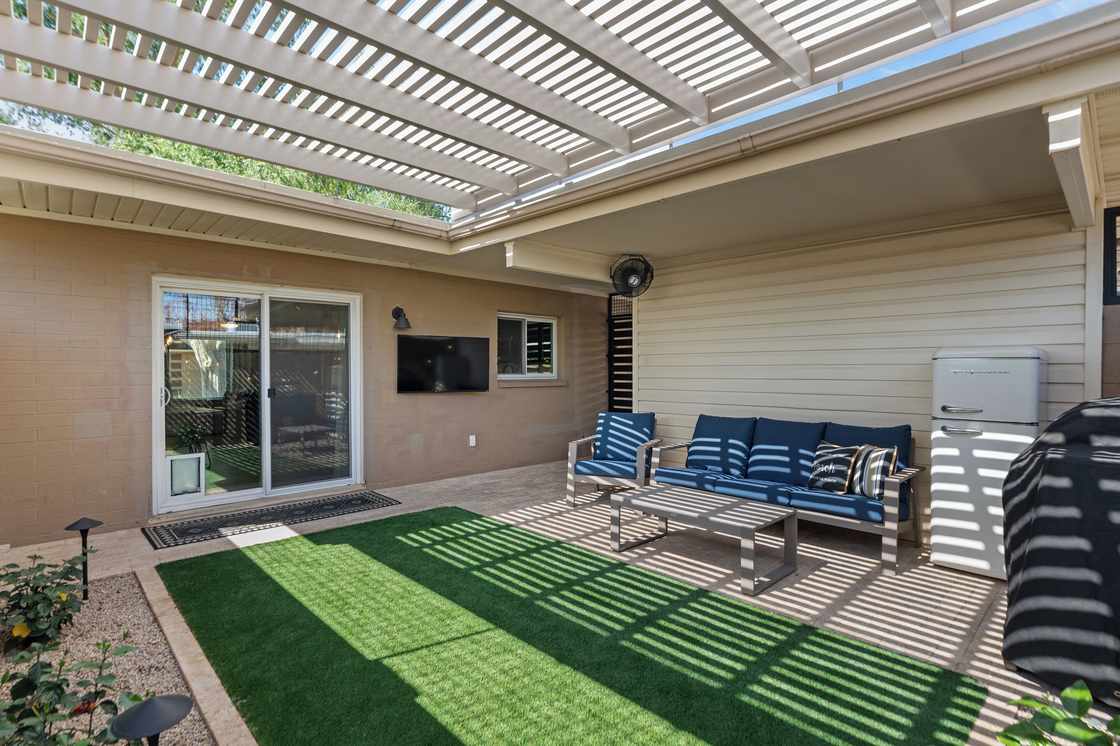 Une terrasse couverte avec une porte-fenêtre coulissante, un canapé bleu et un ventilateur de plafond.
