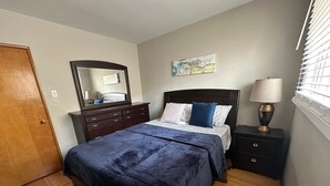 A bedroom with a bed, dresser, nightstand, lamp, and a window with blinds. - Winnipeg Spotless cozy 4-bedroom home (Winnipeg)
