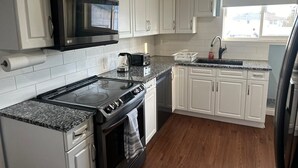 A modern kitchen with white cabinets, a stainless steel stove, a microwave, and a sink. - Winnipeg Spotless cozy 4-bedroom home (Winnipeg)