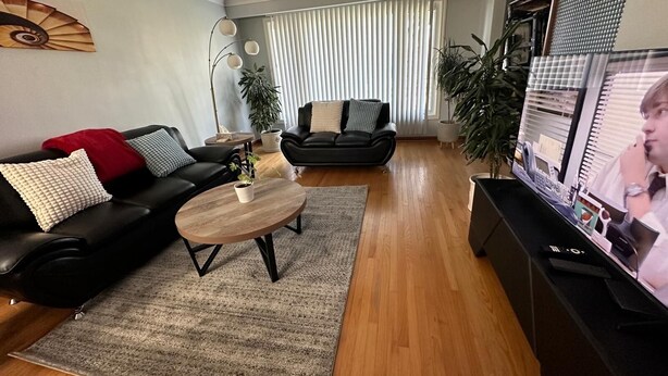 A modern living room with a black leather sofa, a wooden coffee table, and a television on a stand. - Winnipeg Spotless cozy 4-bedroom home (Winnipeg)