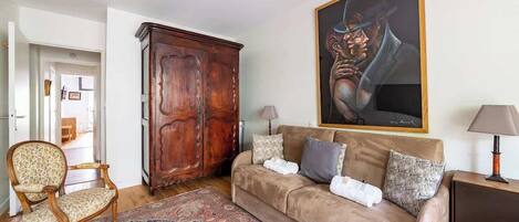 A living room with a sofa, a wooden cabinet, a chair, a rug, and a painting on the wall.