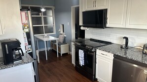 A compact kitchen with white cabinets, a black microwave, a stove, and a dishwasher. - Winnipeg spotless Cozy 3 bedrooms home (Winnipeg)