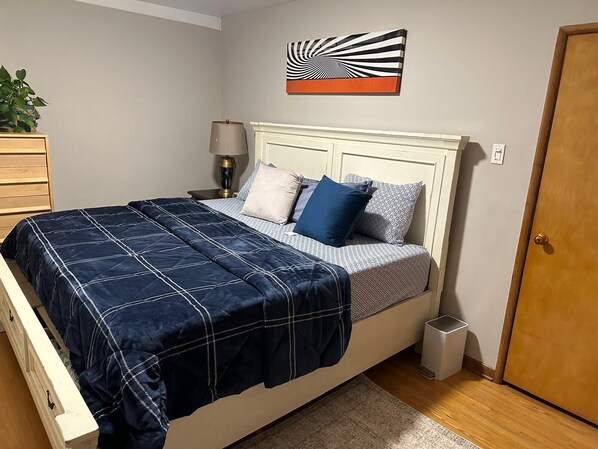 A neatly made bed with a blue quilt, a bedside lamp, and a wall art piece above it.