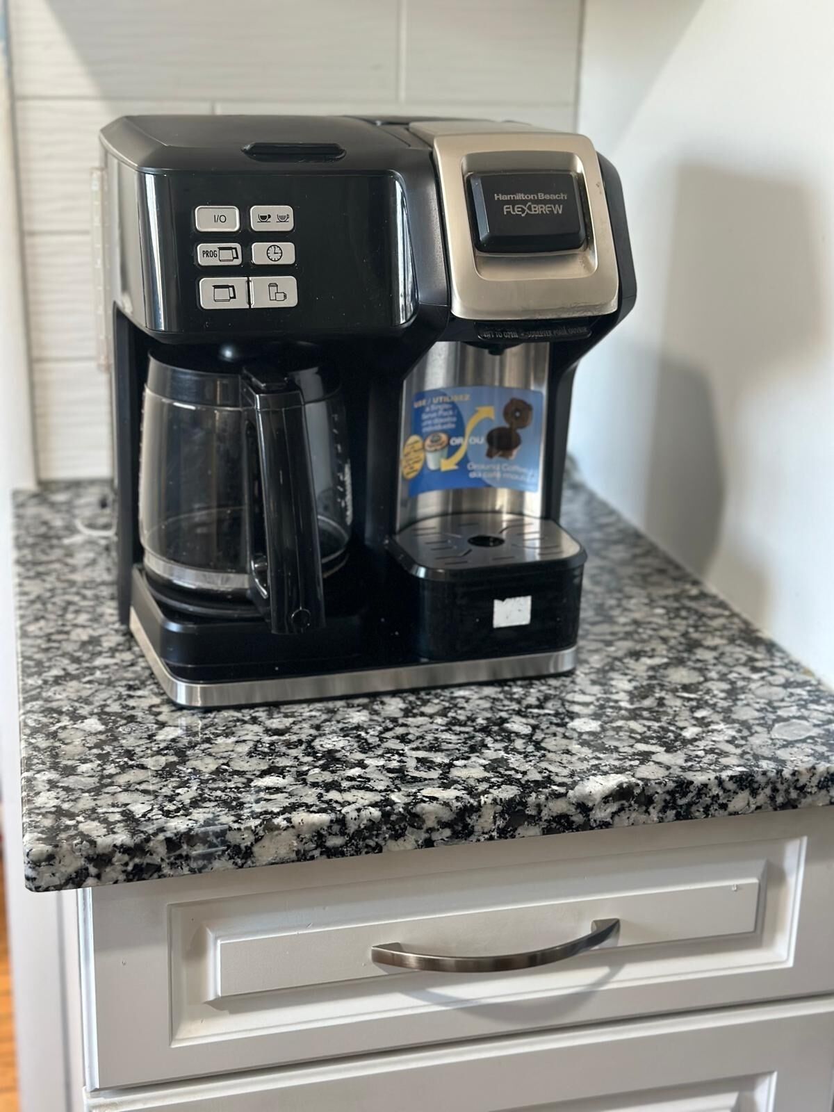 Una cafetera Hamilton Beach FlexBrew damunt un taulell de granat, a prop d'un calaix blanc.