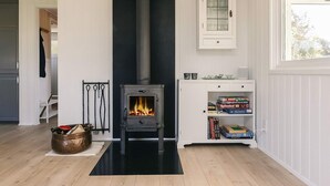 Una sala de estar moderna con chimenea de leña, paredes blancas y un ventanal.